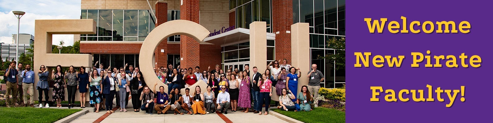 A group of new faculty members standing around the large ECU letters outside the Main Campus Student Center